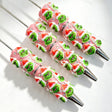 Close-up of four pink beadable pens featuring a green cartoon character wearing a Santa hat and clear rhinestones. Equipped with silver metal tips. Ideal for DIY beadable pen projects, focal beads, and handmade holiday crafts.