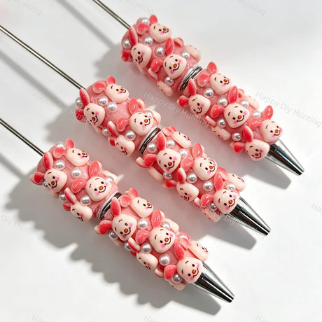 Close-up of four pink pig cartoon character beadable pens on a white background. Each pen features pink beads decorated with pig faces and white faux pearls, paired with silver metal tips. Ideal for DIY beadable pen projects, focal beads, and pen toppers.