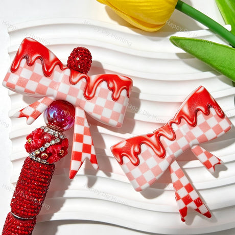Silicone bow beads featuring a pink and white gingham pattern with a glossy red drip finish. Soft, durable, and flexible, perfect for beadable pens, keychains, and handmade crafts.
