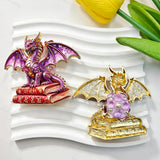 Purple book winged dragon metal fancy bead with rhinestones shown from the front and back. The front features a detailed purple dragon with enamel wings sitting on red books, while the back shows a gold metal finish. Perfect for DIY beadable pens and crafts.