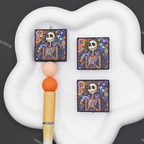 Vibrant colorful floral swirl square silicone focal beads featuring a decorative skeleton, ideal for Halloween beadable pens, keychains, goth and Day of the Dead handmade craft accessories.
