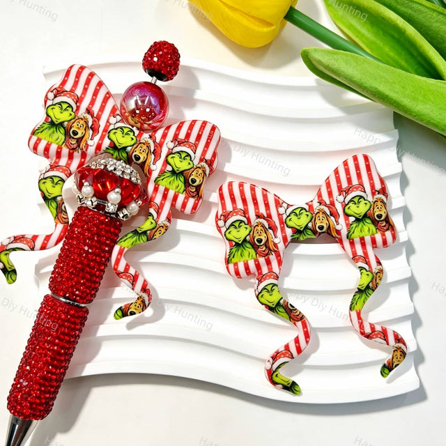 Red striped bow-shaped silicone focal beads featuring a festive Christmas character print design. Soft, durable, and flexible, perfect for beadable pens, keychains, and handmade holiday crafts.