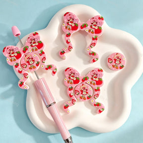 Bow-shaped silicone focal beads featuring a cute strawberry girl character print design. Soft, durable, and flexible, perfect for beadable pens, keychains, and handmade crafts.