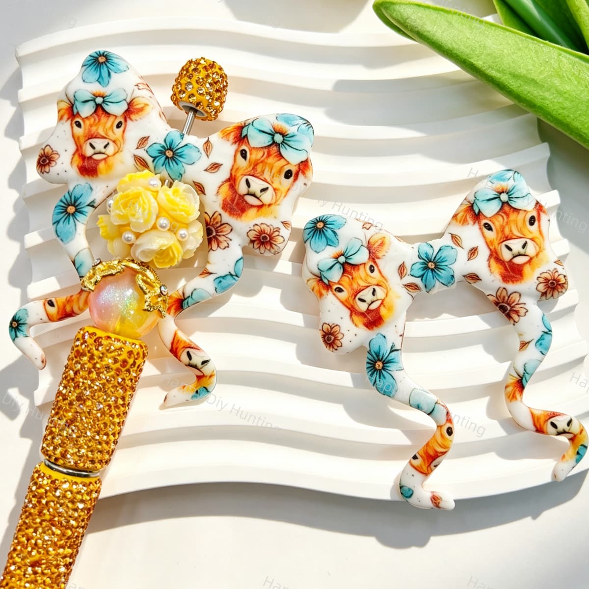 Teal highland cow floral print silicone bow beads displayed with a gold rhinestone beadable pen. Featuring an adorable highland cow with a bow and teal flowers. Soft, durable, and perfect for beadable pens, keychains, and handmade crafts.