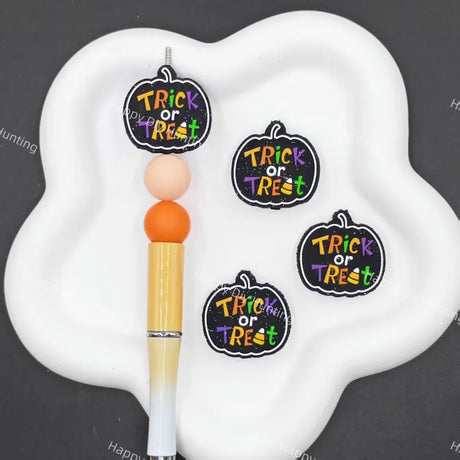 Three pumpkin-shaped 'Trick or Treat' stickers displayed on a white cloud-shaped tray next to a yellow and white pen, set against a dark gray background.