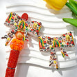 Bow-shaped silicone focal beads featuring a vintage tattoo style religious figure, red roses, cactus, and decorative elements on a white background. Soft, durable, and flexible, perfect for beadable pens, keychains, and handmade crafts.