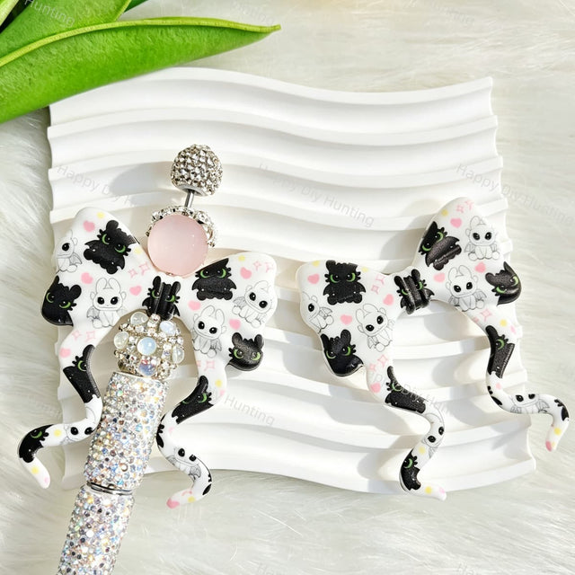 White bow-shaped silicone focal beads featuring a cute cartoon dragon design. Soft, durable, and flexible, perfect for beadable pens, keychains, and handmade crafts.