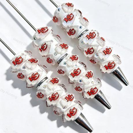 Close-up of four white beadable pens featuring a red football team logo on white translucent beads, accented with clear rhinestones and silver metal tips. Perfect for DIY beadable pen projects, sports gifts, and handmade crafts.