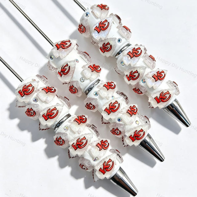 Close-up of four white beadable pens featuring a red football team logo on white translucent beads, accented with clear rhinestones and silver metal tips. Perfect for DIY beadable pen projects, sports gifts, and handmade crafts.