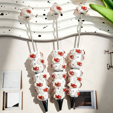 Three white beadable pens featuring a red football team logo on white translucent beads, accented with clear rhinestones and silver metal tips. Displayed on a white wavy tray. Ideal for DIY beadable pen projects, sports gifts, and handmade crafts.