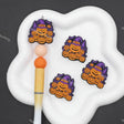 Three Halloween-themed embroidered patches featuring jack-o'-lanterns under a purple witch hat, displayed on a white cloud-shaped stand alongside a paintbrush on a dark gray background.