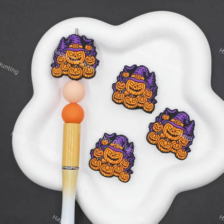 Three Halloween-themed embroidered patches featuring jack-o'-lanterns under a purple witch hat, displayed on a white cloud-shaped stand alongside a paintbrush on a dark gray background.