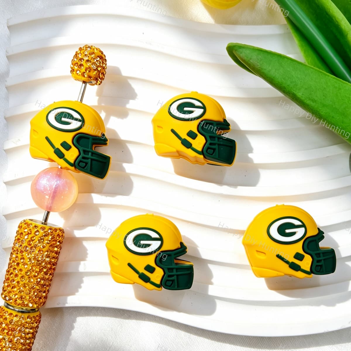 Four yellow and green 3D football helmet silicone focal beads displayed with a gold rhinestone beadable pen. Soft, durable, and flexible, perfect for sports-themed beadable pens, keychains, and handmade crafts.