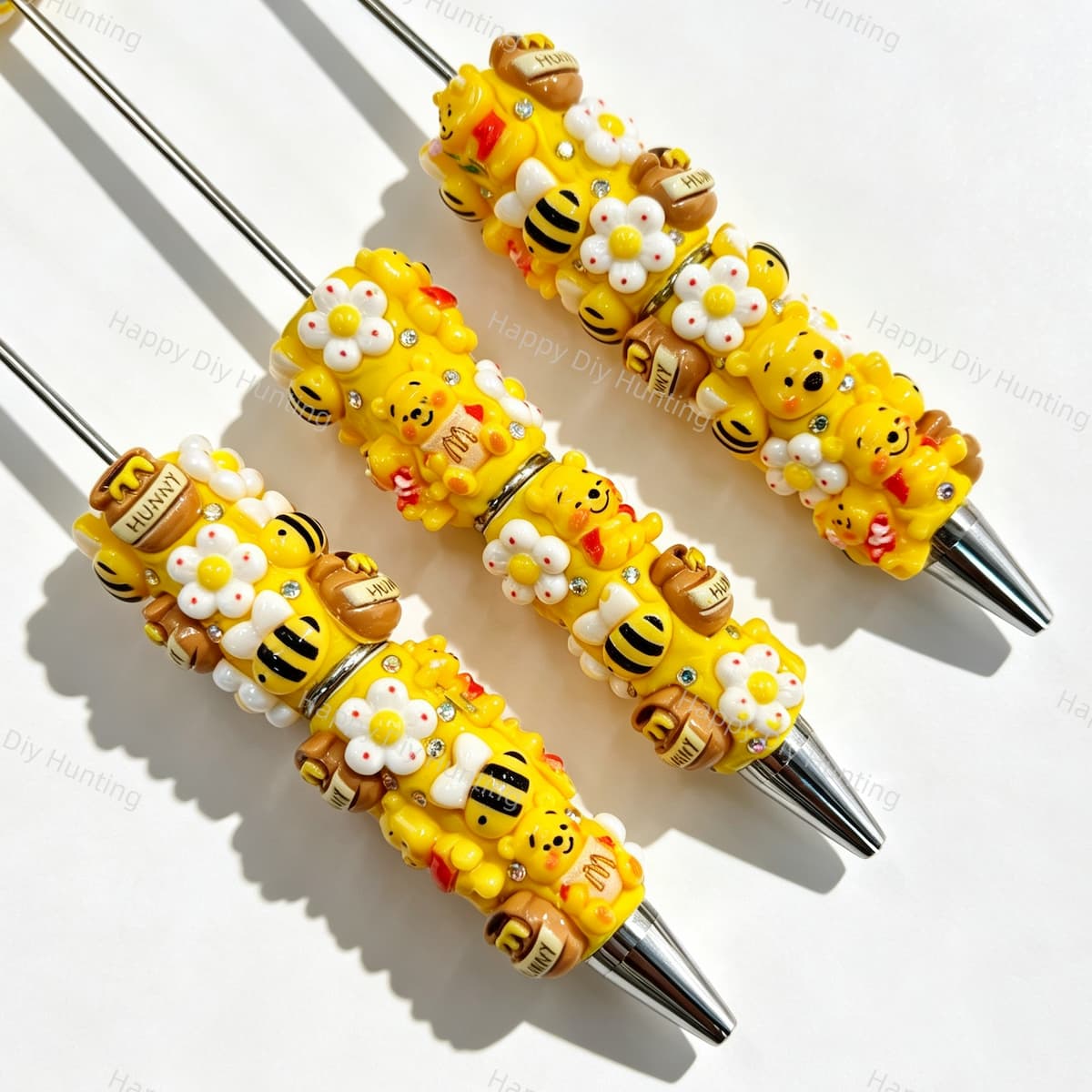 Close-up of four yellow bear cartoon character beadable pens on a white background. Each pen features yellow beads decorated with bear faces, honey pots, bees, white flowers, and clear rhinestones, paired with silver metal tips. Ideal for DIY beadable pen projects, focal beads, and pen toppers.