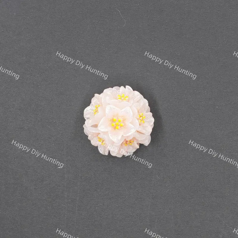 A small white and pale pink flower-shaped accessory with yellow centers, photographed on a dark gray textured background with repeated Happy DIY Hunting watermarks.