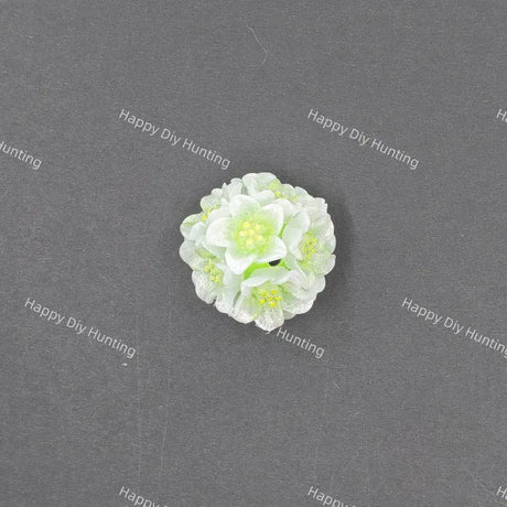 A small white and light green artificial flower craft embellishment, photographed from above on a dark gray textured background with repeating 'Happy DIY Hunting' watermarks.