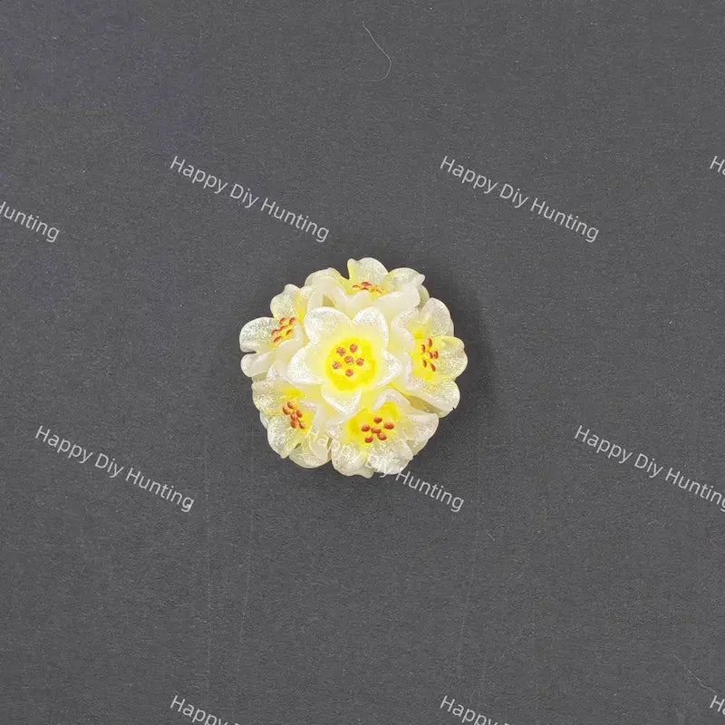 A small white and yellow flower-shaped bead or charm with orange-red speckles, centered on a dark gray background with repeated 'Happy DIY Hunting' watermark text.