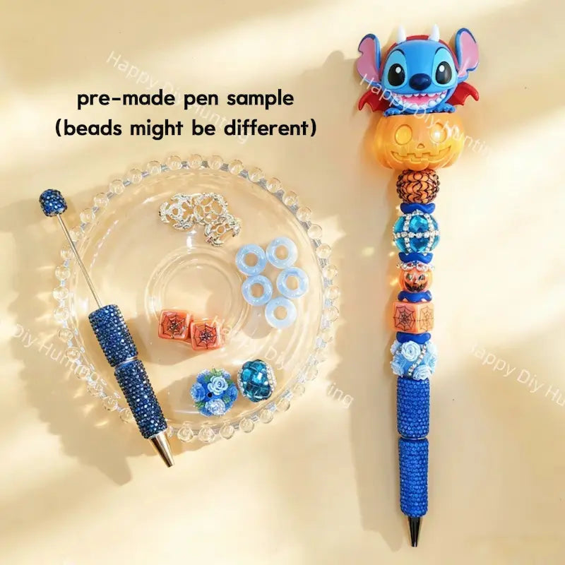 Pre-made beaded pen featuring a blue cartoon monster character sitting inside an orange Halloween pumpkin topper, decorated with blue rhinestone beads and pumpkin charms.